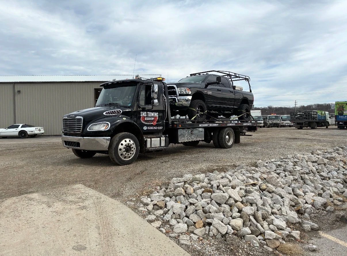 SNS Towing black flatbed truck carrying a black RAM pickup at the Arnold, MO yard